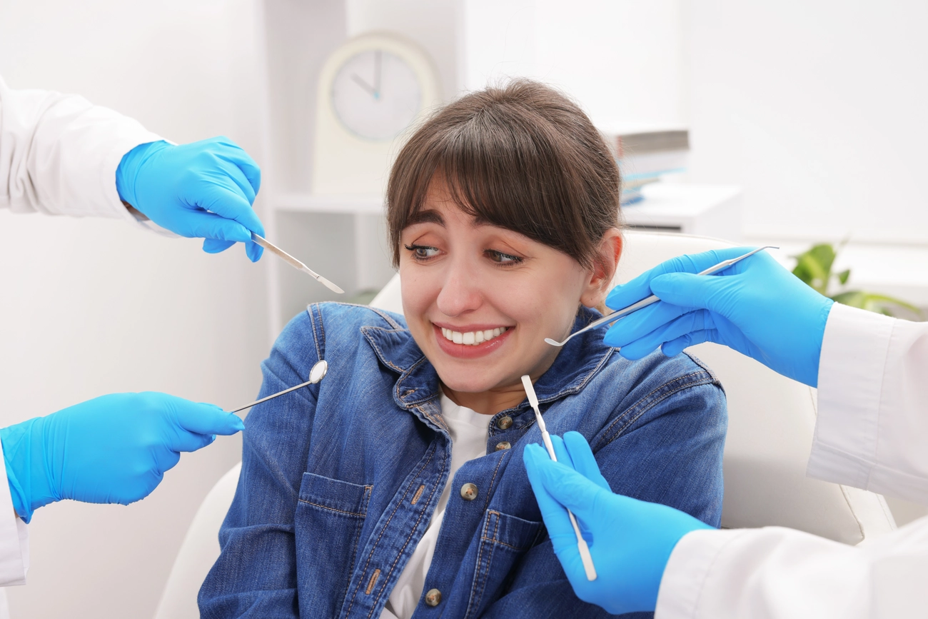 EQ Smile - Zahnarztpraxis - Verängstigte Frau mit Termin beim Zahnarzt und Assistentin in der Klinik